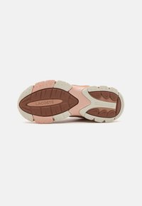 Semelle de chaussure Lacoste incluant une combinaison de caoutchouc rose clair et marron, surface texturée avec des crans, et détail de logo en relief.