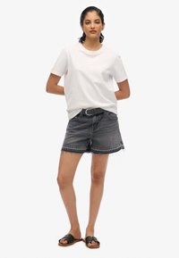 T-shirt blanc en coton, shorts en denim noir avec des bords effilochés et des sandales noires. Tenue simple et décontractée avec un design épuré.