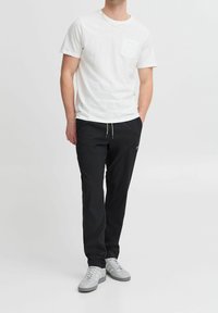 Hvid t-shirt med korte ærmer og brystlomme, parret med sorte bukser med elastisk talje og snørre, afsluttet med grå sneakers.