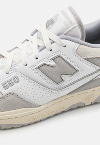 Bílé kožené tenisky s šedými semišovými a síťovanými doplňky, perforovanými detaily a plastickým logem "N" s označením "550" na straně.