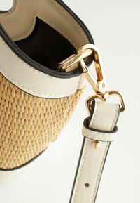 Gros plan d'un sac en paille tressée avec une bordure en cuir blanc et une sangle attachée par une boucle en métal doré.