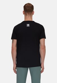 Zwarte katoenen T-shirt met korte mouwen, voorzien van een vierkante logopatch op de bovenrug. Gladde textuur met een klassieke pasvorm.