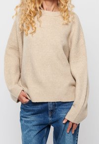 Beige pruhovaný svetr s volným střihem, širokými rukávy a kulatým výstřihem. V kombinaci s modrými džíny.