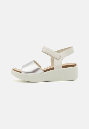 Wedge sandal with a metallic silver toe strap and white adjustable ankle strap. Features a natural cork footbed and a textured white sole.