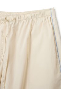 Pantalones cortos de color crema claro hechos de una tela suave; cuentan con una cinturilla elástica con cordón y un detalle de raya lateral azul claro.