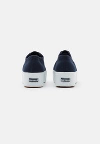 Paire de baskets compensées en toile bleu marine avec semelles blanches, vues de dos, montrant l'étiquette de la marque "Superga" sur chaque talon.