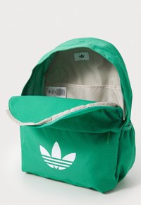 Πράσινο σακίδιο πλάτης με το λευκό λογότυπο trefoil της Adidas, κατασκευασμένο από ανθεκτικό ύφασμα, με μεγάλη κύρια θήκη και αναδιπλούμενο καπάκι.