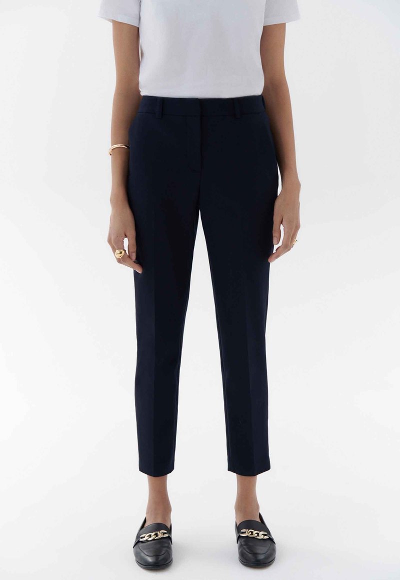 Marintröjor med smal passform, med flat front, osynliga sidofickor och en mjuk textur. I kombination med svarta loafers.