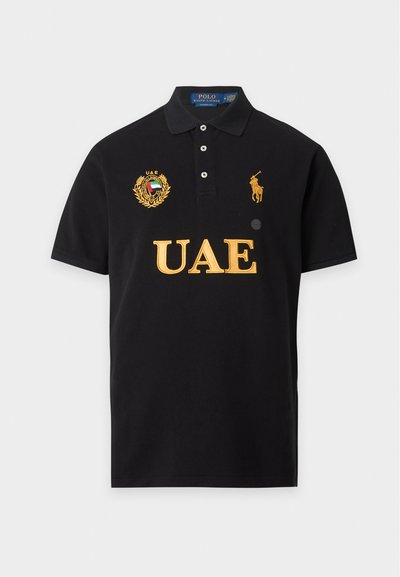 Μαύρο πόλο με κίτρινο κείμενο "UAE", έμβλημα UAE στο αριστερό στήθος και κίτρινο λογότυπο Polo Ralph Lauren στο δεξί στήθος.
