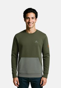 Sweatshirt vert olive avec une poche grise contrastante, présentant des poignets côtelés, un col rond et un logo discret sur la poitrine. Texture de tissu lisse.