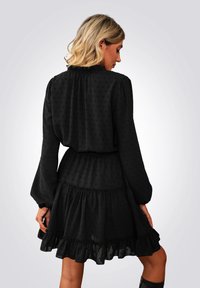 Vestido negro con lunares texturizados, mangas largas, un dobladillo con volantes y una cintura elástica para un ajuste cómodo.