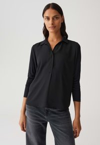 Maglietta nera a maniche lunghe con colletto, tessuto morbido e vestibilità comoda. Abbinata a jeans grigio scuro per un look casual.