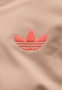 Κόκκινο κεντημένο λογότυπο Adidas trefoil σε ροζ υφασμάτινη υφή, κεντραρισμένο και καθαρά ορατό.