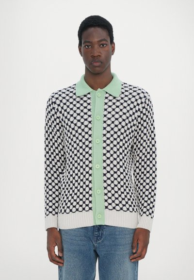 Cardigan tricotat cu un model din puncte crem și bleumarin, guler verde și nasturi. Mâneci lungi, manșete și tiv elastice, croială casual.