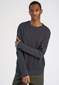 Maglione a coste navy con colletto rotondo e maniche lunghe; presenta polsini allungati e una vestibilità comoda. Texture liscia.