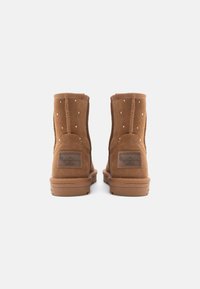 Καφέ σουέτ ankle boots με διακοσμητικά καρφιά, στρογγυλή μύτη και λογότυπο στο πίσω μέρος. Ανθεκτική ελαστική σόλα για πρόσφυση.