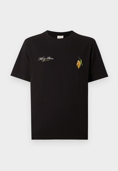 Μαύρο T-shirt με στρογγυλή λαιμόκοψη, λευκό κείμενο "Filling Pieces 'Baking Bread'" στο αριστερό μέρος του στήθους και μικρές κεντητές κίτρινες και πράσινες πιπεριές τσίλι στο δεξί μέρος του στήθους.
