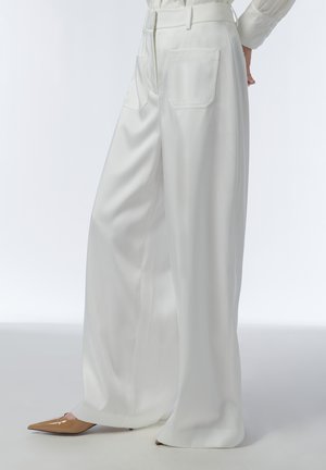 Witte wijde broek met achterzakken, gedragen met beige pumps met puntige neus en een wit langermig topje dat in de broek is gestopt.