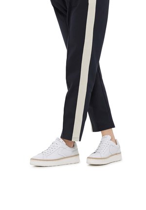 Hvide lædersneakers med en tekstureret overflade og en tyk, lys sål. Båret med navybukser, der har en cremefarvet vertikal stripe.