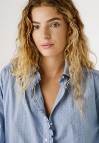 Hellblaues, kariertes Hemd mit Rü schenkragen, langen Ärmeln und weißen Knöpfen. Der Stoff wirkt weich und leicht strukturiert.