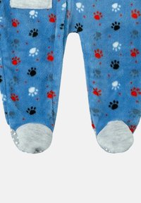 Pijama de forro polar azul con un patrón de huellas en rojo, negro, gris y blanco por toda la prenda. Incluye un bolsillo blanco y suelas suaves en gris.
