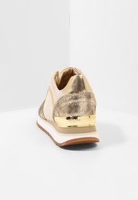 Sneaker z teksturowanym, jasnobeżowym wierzchem, metalicznie złotymi akcentami i grubą białą podeszwą. Posiada błyszczący złoty zapiętek z brandingiem.