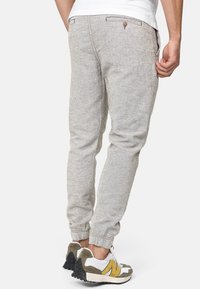 Joggers de color gris claro, hechos de tejido texturizado, con puños elásticos, dos bolsillos traseros con cierre de botón y un corte relajado.