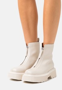 Botas de tobillo de cuero blanco con suela de goma gruesa, que cuentan con una cremallera frontal y detalles acanalados en la suela. Textura suave y diseño sencillo.