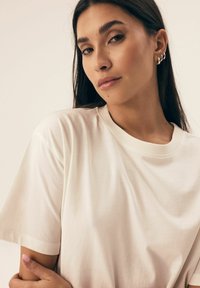 Jasno beżowa bawełniana koszulka z klasycznym okrągłym dekoltem, luźnym krojem i krótkimi rękawami, o gładkiej fakturze i subtelnym połysku.