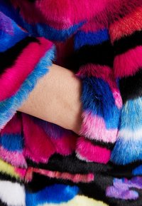 Nepal wollen coat met levendige roze, blauwe en zwarte strepen. Zachte textuur met een kleurrijk patroon nabij de manchetten, dat meerdere tinten toont.