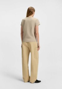 Beżowa dopasowana koszulka z krótkim rękawem, w połączeniu z luźnymi beżowymi spodniami cargo z dużymi bocznymi kieszeniami i gładką teksturą.