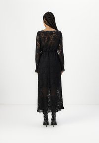 Μαύρο δαντελένιο φόρεμα με μακριά μανίκια, διάφανο υλικό, φλοράλ σχέδιο, ημιδιαφάνεια στο στρίφωμα, στενή μέση και συνδυασμένο με μαύρες μπότες με τακούνι.