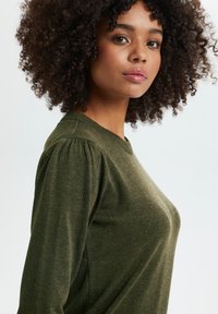 Olivgrüner, gestrickter Pullover mit Rundhalsausschnitt und puffigen Ärmeln, mit einer weichen Textur und einer figurschmeichelnden Silhouette.