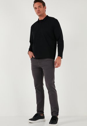 Camisa polo negra de manga larga con cuello, combinada con jeans slim-fit gris oscuro y zapatillas negras con detalles texturizados.