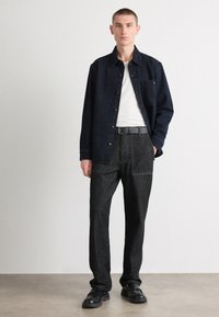 Camisa de ganga azul escura, estilo de botão, usada sobre um top branco. Calças largas cinzas com bolsos frontais. Sapatos pretos.