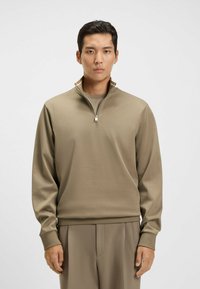 Beige zip-up pullover made of soft fabric with a stand collar. Features long sleeves and a relaxed fit. Textured material with subtle sheen.