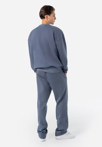 Grå sweatshirt og matchende sweatpants, begge lavet af blødt stof, med en afslappet pasform og ribbede manchetter. Sneakersene er hvide.