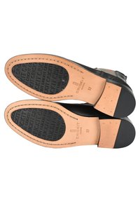 Semelles de chaussures en cuir noir avec un intercalaire en cuir tan. Le caoutchouc texturé au fond présente un motif "CRICKIT". Taille 37 marquée sur le côté.