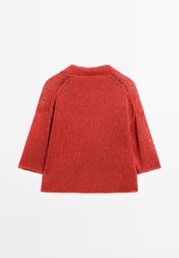 Rode gebreide trui met een hoge halslijn, losse mouwen en open geweven details, die een gevarieerd patroon door de stof toont.