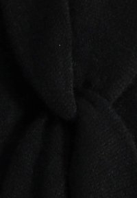 Tissu noir avec une surface douce et texturée dégageant un motif noué. Le matériau semble dense et légèrement duveteux.