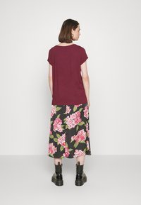 Top de manga curta vinho combinado com uma saia midi preta floral, com grandes flores cor-de-rosa e folhas verdes. Usada com botas de tornozelo pretas.