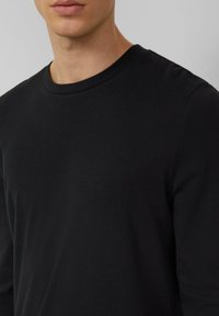 Czarna koszulka z długim rękawem wykonana z gładkiej bawełnianej tkaniny, z prążkowanym, okrągłym dekoltem i luźnym krojem, bez widocznych wzorów ani akcentów.