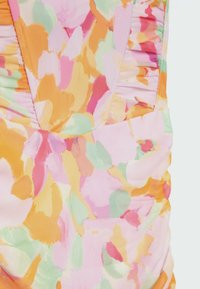 Gros plan sur un tissu avec un motif floral abstrait en rose pastel, orange, jaune, vert et violet, présentant des détails froncés et cousus.