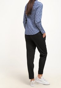 Ljusblå skjorta med knappar och små mörka mönster, matchad med svarta tajta byxor och vita sneakers. Materialet verkar slätt och avslappnat.