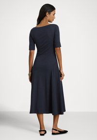 Tamno mornarsko plava haljina do koljena s pripijenim gornjim dijelom, proširenim suknjom i kratkim zavrnutim rukavima. Glatki materijal sa blagim rastezanjem.