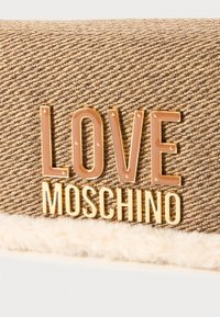 Brun teksturert stoffveske med plysjkant, med dristig "LOVE MOSCHINO"-bokstaver i gull og lys brun.