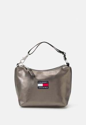 Kleine metalen bronzen handtas met zwarte verstelbare band en Tommy Jeans-logo patch aan de voorkant in het midden.