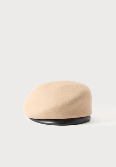 Béret en laine beige avec un bandeau lisse en cuir noir à la base, présenté sur un fond gris clair uni.