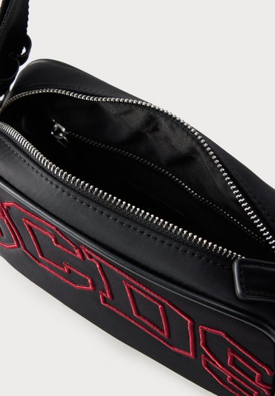 Μαύρο τσαντάκι χιαστί με φερμουάρ, με κόκκινη κεντημένη επιγραφή "MOSCHINO" και ορατά ασημί δόντια φερμουάρ, που δείχνει το ανοιχτό κύριο διαμέρισμα.