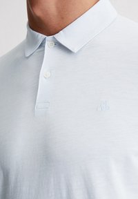 Jasnoniebieska koszulka polo z miękkiego, teksturowanego materiału, z dwoma guzikami przy kołnierzyku oraz haftowanym logo w dopasowanym kolorze.